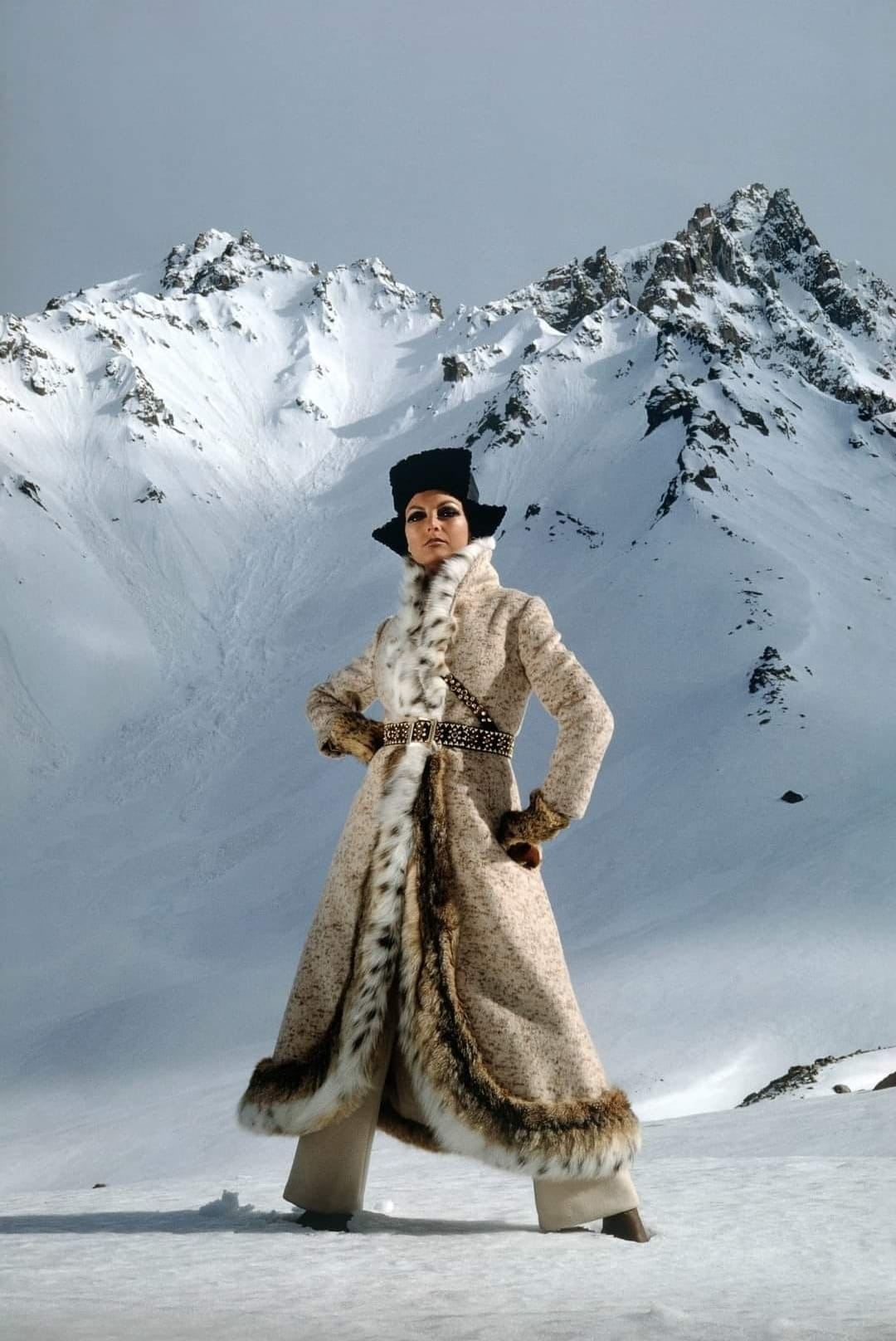 Model wearing a heavy, fur-lined Afghan coat in the snowy mountains.